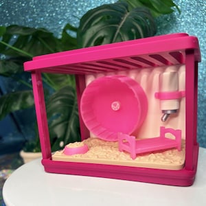 May include: A bright pink plastic pet cage featuring a circular exercise wheel with a paw print center, a small pink bed, a matching pink food bowl, and a white water bottle with a metal spout, all set on a textured beige floor base.
