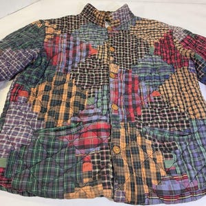 May include: A quilted jacket featuring a patchwork design composed of various plaid and checkered fabric squares in shades of red, green, blue, yellow, and black. The garment includes a high collar, long sleeves, and a front button closure.