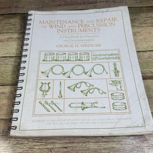 May include: A spiral-bound book titled "Maintenance and Repair of Wind and Percussion Instruments" by George H. Springer. The cover features illustrations of various musical instruments in green ink on a cream-colored background.