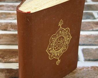 May include: A brown leather-bound book with gold embossed calligraphy on the cover. The book's pages are aged, and the spine is visible. The book is set against a brick background.