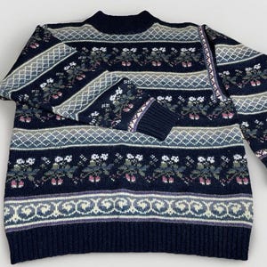 May include: A navy blue sweater with a mock neck and long sleeves. The sweater features a floral and geometric pattern in white, green, and purple. The cuffs and hem are ribbed.