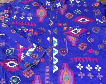 May include: A button-down shirt in a vibrant blue hue, adorned with a Southwestern-inspired pattern. The design features geometric shapes in shades of purple, orange, and white. The shirt has two chest pockets and long sleeves.