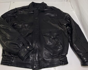 May include: A black leather bomber jacket with a collared neckline, two front pockets, and a ribbed hem and cuffs. The jacket has a small emblem on the chest and buttoned cuffs. The leather appears to be slightly distressed.