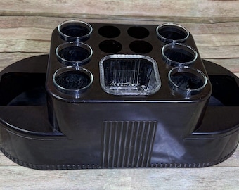 May include: A vintage black bar caddy with a rectangular ice bucket, eight glass holders, and two side compartments. The caddy has a curved oval base and brass-colored handles. The design is reminiscent of the Art Deco era.