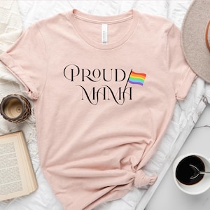 May include: A pink t-shirt with the text "PROUD MAMA" in black script with a rainbow pride flag to the right of the text.