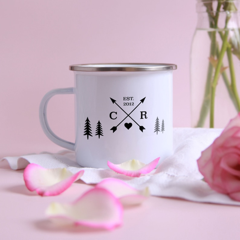May include: White enamel camping mug with black lettering that reads "EST. 2012" and "C & R" with arrows and a heart in between. There are also small pine trees on either side of the design.