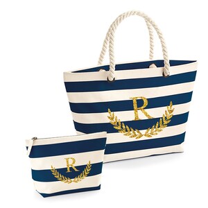 May include: A blue and white striped canvas tote bag with a gold glitter initial "R" surrounded by a gold glitter laurel wreath. A matching smaller zippered pouch with the same design is included.