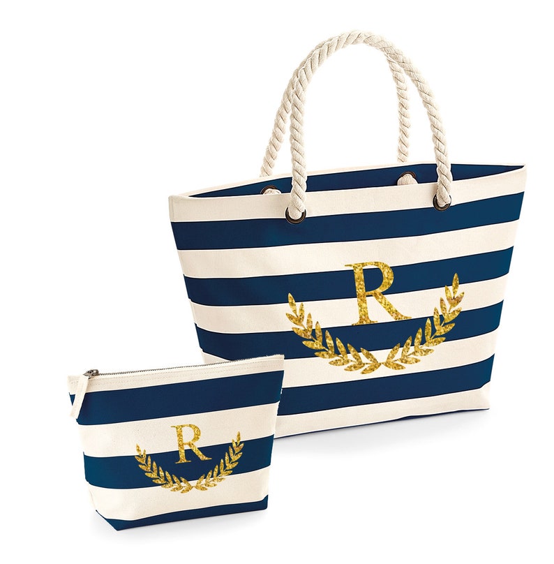 May include: A blue and white striped canvas tote bag with a gold glitter initial "R" surrounded by a gold glitter laurel wreath. A matching smaller zippered pouch with the same design is included.