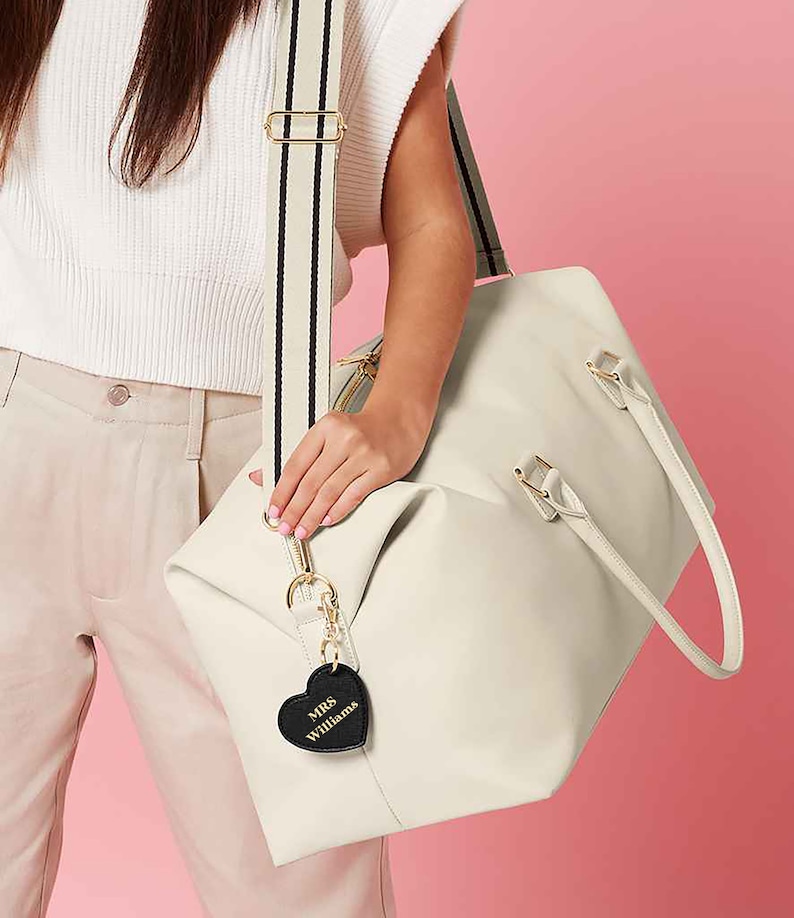 May include: A white leather travel bag with black accents and a black heart-shaped luggage tag that says "MRS Williams".