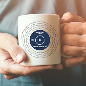 May include: White ceramic mug with a blue and white record design. The mug features the song title "Can't Take My Eyes Off You" and the lyrics to the song. The mug is personalized with the names "Jonathan & Suzy" and the date "12th May 2022".