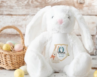 May include: White plush bunny rabbit with a blue and gold embroidered patch that says "Olivia my first easter".