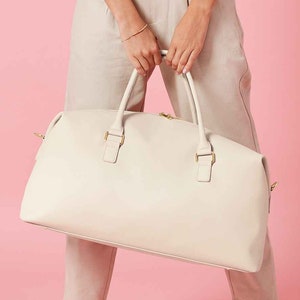 May include: A cream-colored leather duffel bag with gold hardware and a zipper closure.