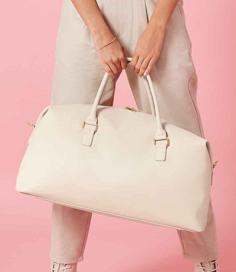 May include: A cream-colored leather duffel bag with gold hardware and a zipper closure.