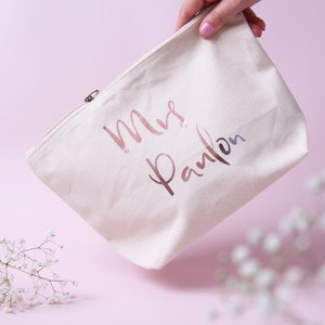 May include: A white canvas zippered pouch with the text "Mrs. Paulson" in rose gold foil lettering.