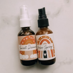 May include: Two amber glass spray bottles with white and black spray tops. The bottles have colourful rainbow labels with the text "Sweet Dreams" and "Germ Spray".