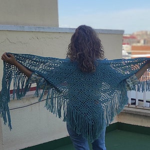 Peut inclure: Un châle en crochet bleu sarcelle avec des franges. Le châle est drapé sur les épaules d'une personne.