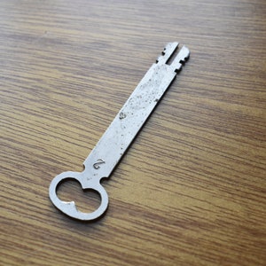 May include: A silver-colored metal key with a unique, rounded head and a long, straight shaft. The key has a number "2" etched on the shaft.
