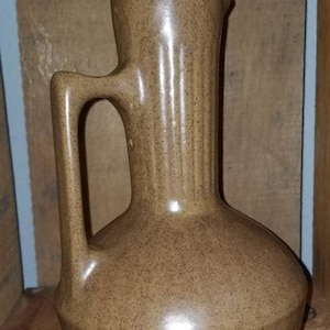 Puede incluir: Una jarra de cerámica marrón con un esmalte moteado y un diseño acanalado. La jarra tiene un pico y una asa.