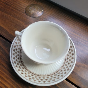 May include: A white teacup and saucer with a brown floral pattern. The saucer has a fluted edge.