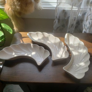May include: Three white ceramic serving dishes shaped like a crescent moon. The dishes are arranged on a wooden surface.