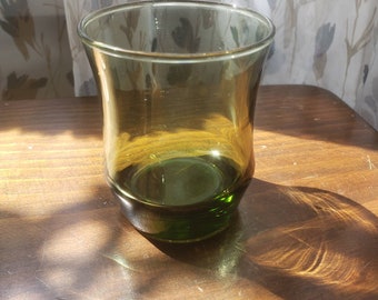 May include: A green glass tumbler with a flared lip and a rounded base. The glass is clear and has a slight amber tint.