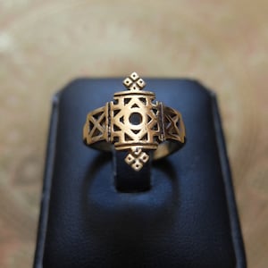 Peut inclure: Une bague en or avec un motif géométrique. La bague est sur un présentoir à bague noir.