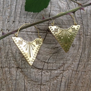 Può includere: Un paio di orecchini a cerchio dorati con un design geometrico triangolare. Gli orecchini sono appesi a un ramo spinoso.