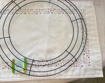 Pode incluir: Um aro de grinalda de metal preto com um padrão de grade, perfeito para artesanato. O aro da grinalda está sobre um descanso de mesa branco com uma borda decorativa. Uma etiqueta verde e branca está presa ao aro da grinalda.