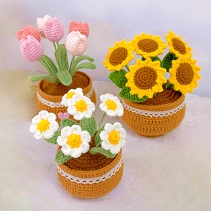 Puede incluir: Tres arreglos de flores de ganchillo en macetas. La primera maceta tiene tulipanes rosas, la segunda girasoles amarillos y la tercera margaritas blancas.