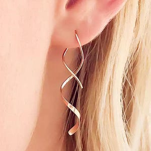 May include: Rose gold spiral earrings. These earrings have a continuous, flowing design that curves and twists, creating a dynamic and elegant look. The earrings are made of a shiny, rose-gold coloured metal, reflecting light and adding a touch of sophistication.
