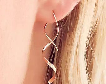 May include: Rose gold spiral earrings. These earrings feature a continuous, flowing design that curves and twists, creating a dynamic and elegant look. The earrings are made of a shiny, rose-gold colored metal, reflecting light and adding a touch of sophistication.