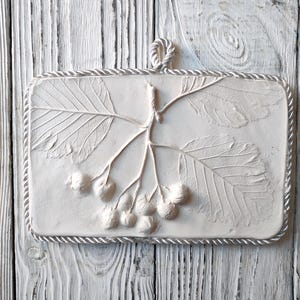 Peut inclure: Décoration murale en plâtre blanc avec un motif en relief de feuilles et de baies. La décoration a une bordure en forme de corde et une boucle pour l'accrocher.