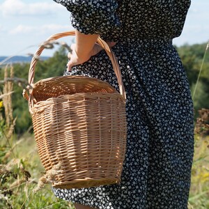 May include: A woman in a black and white floral dress carries a woven wicker basket with a handle.