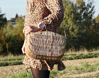 May include: A woman wearing a floral dress and a straw bag with a woven design. She is wearing a watch on her wrist.