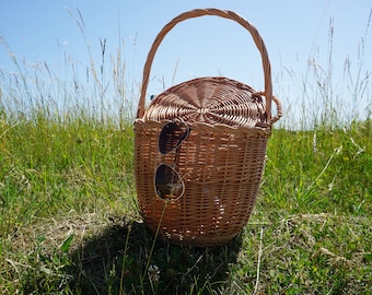 May include: A brown wicker picnic basket with a handle and a lid. Sunglasses are tucked into the basket.