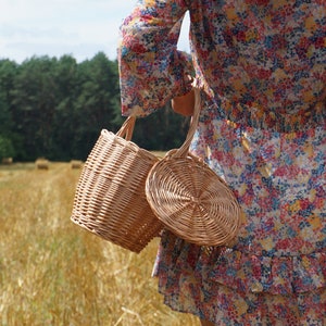 May include: Two wicker baskets, one round and one cylindrical, are held by a person wearing a floral dress. The baskets are made of natural woven material and have a rustic, handmade look.