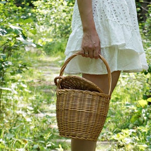 May include: A woman in a white dress carries a woven wicker basket with a handle in a forest setting.