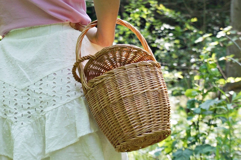 May include: A woven wicker basket with a single handle. The basket is brown and has a natural finish.