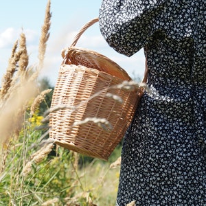 May include: A woman in a black and white floral dress carries a woven wicker basket with a handle.