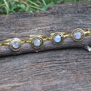May include: Seven gold rings with moonstone settings. The rings are arranged in a row on a wooden surface.