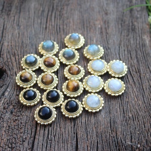 May include: Assortment of gemstone cabochons set in gold tone metal bezels. The stones include tiger's eye, moonstone, labradorite, and black onyx.