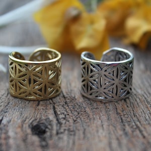 May include: Two silver and gold rings with a flower of life design. The rings are on a wooden surface.