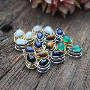 Puede incluir: Surtido de cabujones de piedras preciosas engastados en engastes de tono plateado y dorado. Las piedras incluyen piedra lunar, lapislázuli, ojo de tigre, ónix negro y aventurina verde.