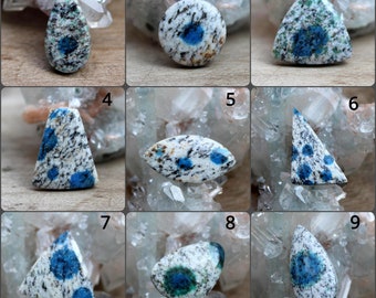 May include: Nine cabochon gemstones with a white base and blue and green flecks. The gemstones are in various shapes, including round, oval, teardrop, and triangular.