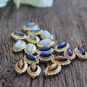 May include: Assortment of gemstone cabochons set in gold tone metal bezels. The stones include moonstone, labradorite, lapis lazuli, tiger's eye, and amethyst.