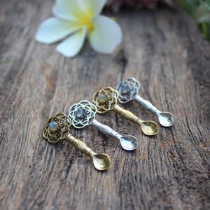 Puede incluir: Cuatro cucharas pequeñas con mangos adornados y una piedra preciosa en el centro de cada mango. Las cucharas están dispuestas en fila sobre una superficie de madera.