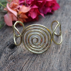May include: A gold-toned metal bracelet with a spiral design. The bracelet is open and has a simple, elegant look.