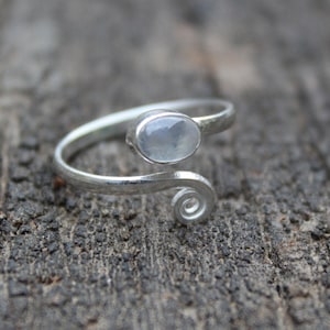 May include: A silver ring featuring a white oval gemstone. The ring band is twisted and has a spiral design.