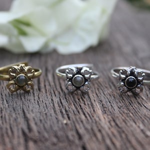 May include: Three silver toe rings with flower designs. The center of each flower has a stone. The stones are gray, gray, and black.