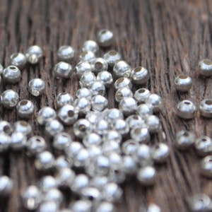 May include: A close-up of a pile of silver metal beads on a wooden surface. The beads are small and round, and they are scattered randomly.